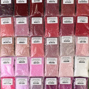 May include: A collection of 24 small plastic bags filled with various colors of tiny round beads. Each bag has a label with the brand name "Preciosa Ornela" and a product code.