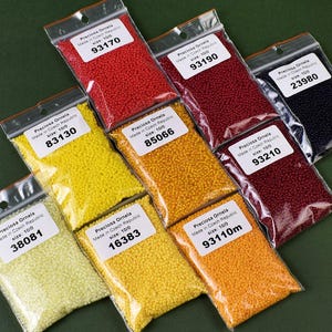 May include: Assortment of small, colorful glass beads in clear plastic bags. Each bag has a label with the brand name "Preciosa Ornela", "Made in Czech Republic", size 10/0, and a number. The beads are in the colors red, yellow, orange, and black.