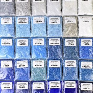 May include: Assortment of small, round, glass beads in various shades of blue, white, and gray. The beads are packaged in clear plastic bags with labels indicating the size and manufacturer, Preciosa Ornela, Made in Czech Republic.