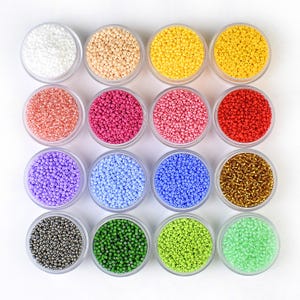 Peut inclure: Vue aérienne de seize petits récipients en plastique transparent remplis de perles de rocaille colorées. Les perles sont de différentes couleurs, dont blanc, beige, jaune, corail, rose, fuchsia, rouge, violet, bleu clair, bleu foncé, or, argent, vert et vert citron.