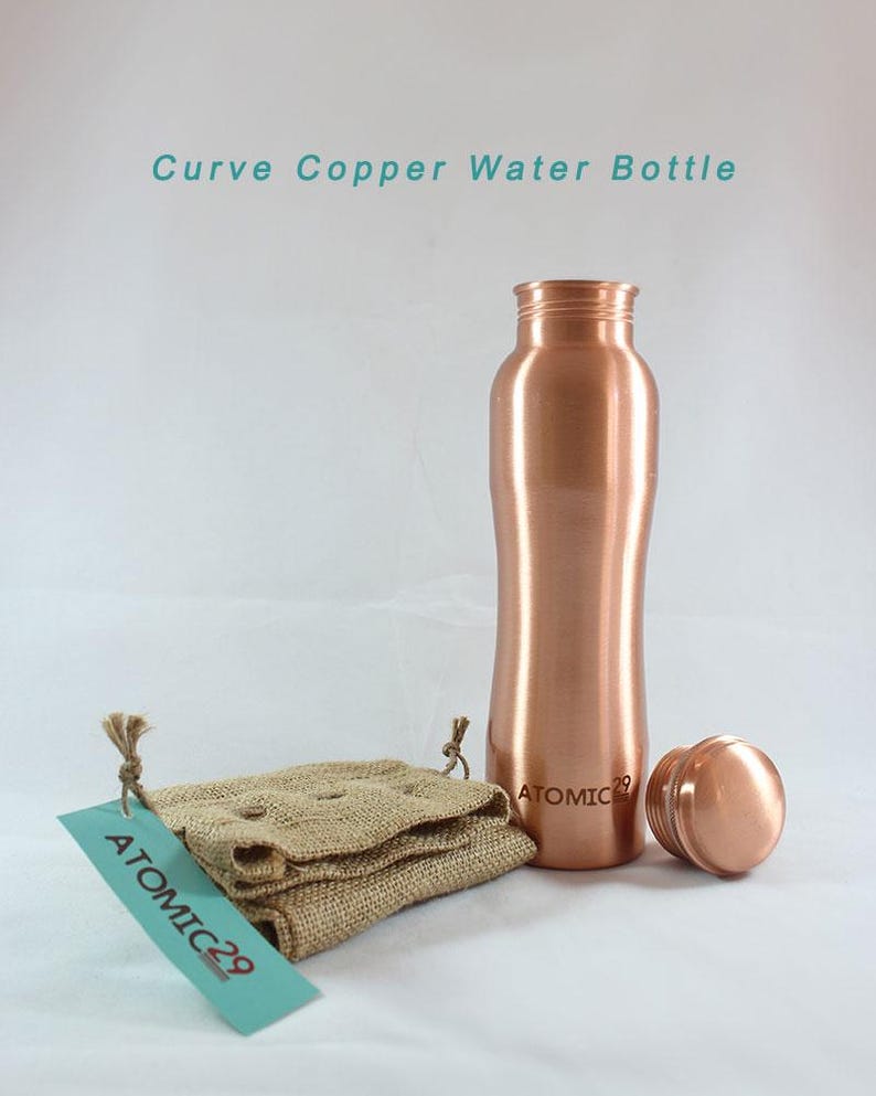 K&ouml;nnte beinhalten: Eine Wasserflasche aus Kupfer mit einem geschwungenen Design. Die Flasche hat einen Deckel und steht auf einer wei&szlig;en Oberfl&auml;che. Die Flasche ist mit "ATOMIC 29" beschriftet.