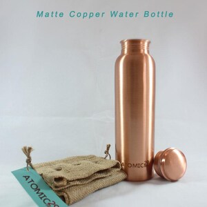 K&ouml;nnte beinhalten: Matte Kupfer-Wasserflasche mit passendem Deckel und einem Jutesack. Die Flasche tr&auml;gt die Gravur "ATOMIC 29" an der Seite.