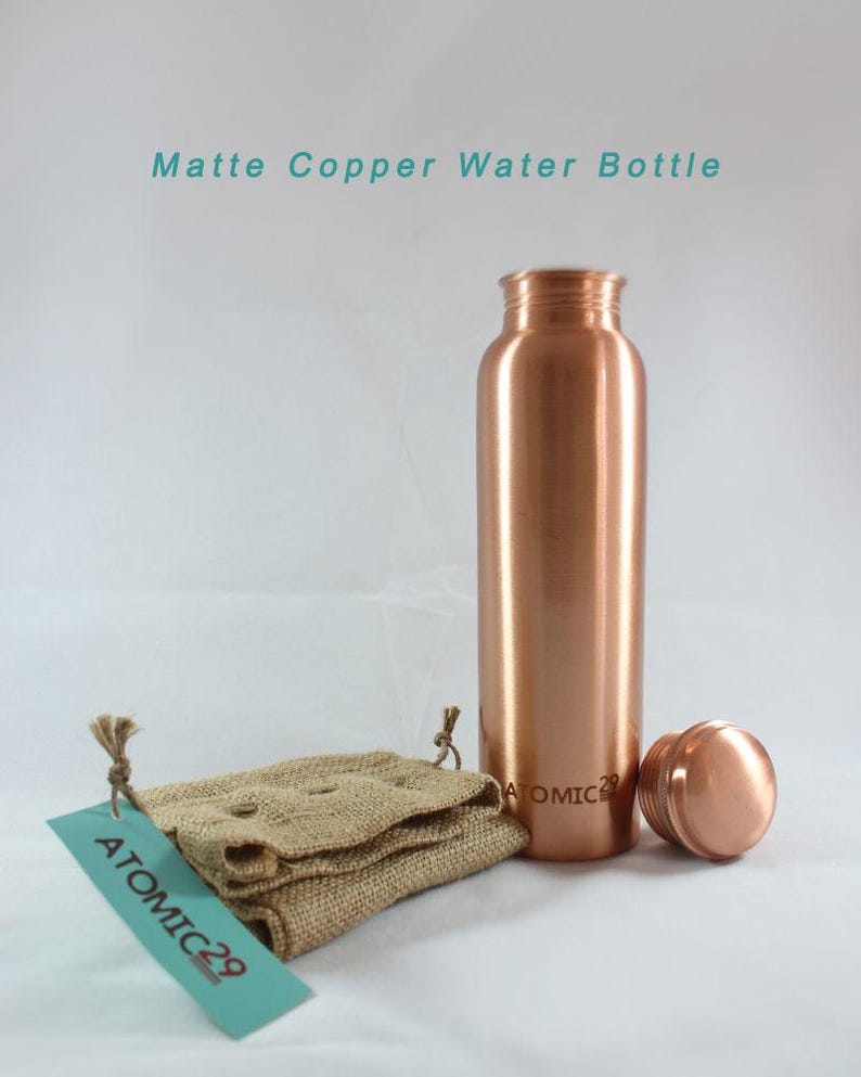 K&ouml;nnte beinhalten: Matte Kupfer-Wasserflasche mit passendem Deckel und einem Jutesack. Die Flasche tr&auml;gt die Gravur "ATOMIC 29" an der Seite.