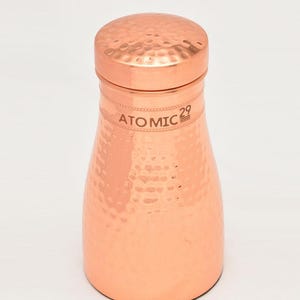 K&ouml;nnte beinhalten: Eine Kupferkaraffe mit geh&auml;mmerter Oberfl&auml;che und einem Deckel. Die Karaffe ist mit "ATOMIC 29" beschriftet.
