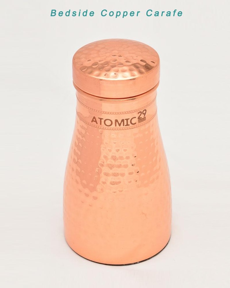 K&ouml;nnte beinhalten: Eine Kupferkaraffe mit geh&auml;mmerter Oberfl&auml;che und einem Deckel. Die Karaffe ist mit "ATOMIC 29" beschriftet.