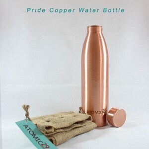 K&ouml;nnte beinhalten: Eine Kupfer-Wasserflasche mit einem Kupferdeckel und einem Jutesack mit einem Etikett mit der Aufschrift "ATOMIC 29". Die Flasche ist mit "ATOMIC 29" beschriftet.