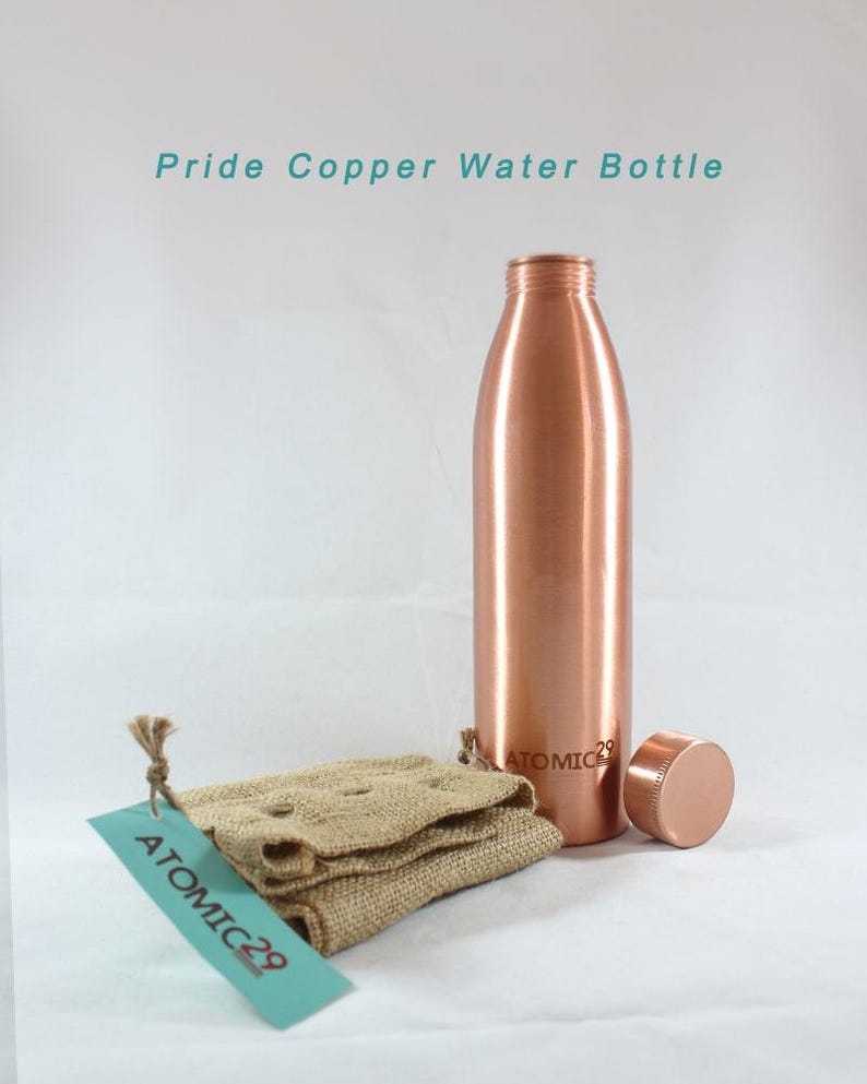 K&ouml;nnte beinhalten: Eine Kupfer-Wasserflasche mit einem Kupferdeckel und einem Jutesack mit einem Etikett mit der Aufschrift "ATOMIC 29". Die Flasche ist mit "ATOMIC 29" beschriftet.