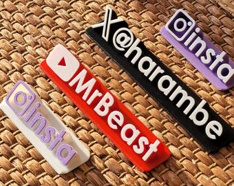 May include: Four colorful plastic name tags with different social media logos and text. The tags are on a woven brown background. The tags read "@harambe", "insta", "MrBeast", and "insta".