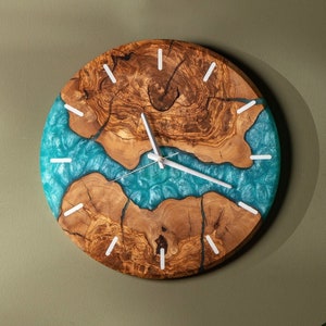 May include: A round wooden clock with a blue resin inlay. The clock face has white hands and white numbers.