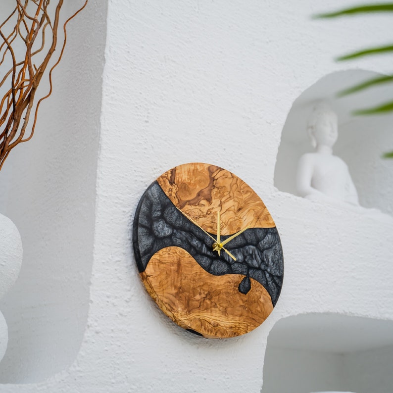May include: A round wooden clock with a black and brown epoxy resin design. The clock has gold hands and a white background.