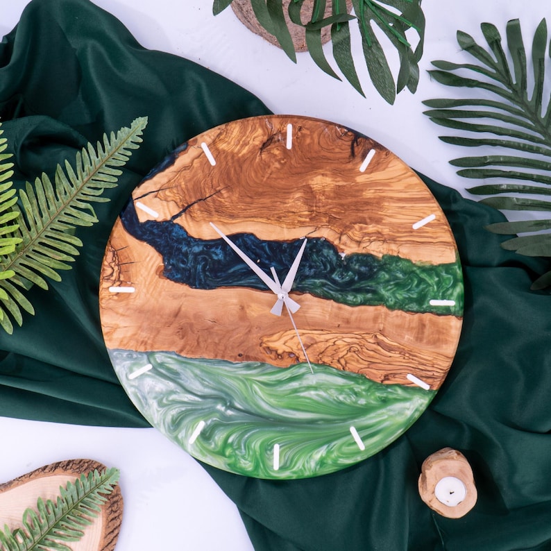 May include: A round wooden clock with a green and blue resin inlay. The clock face has white hands and white numbers.