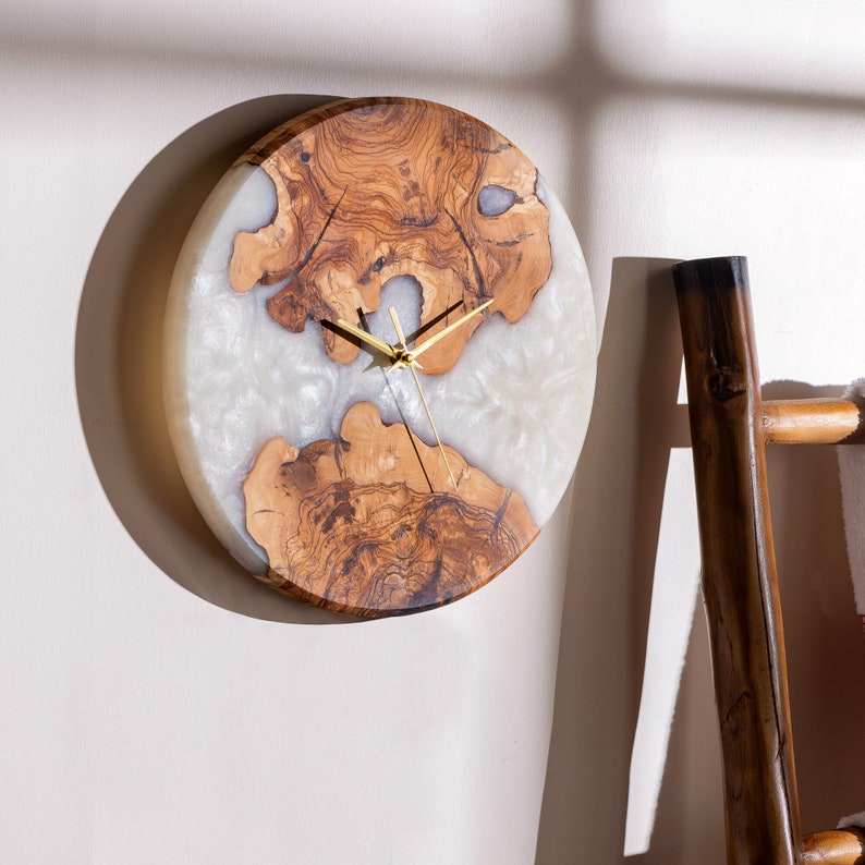 May include: A round wall clock with a white resin face and a wood grain border. The clock has gold hands and a simple design.