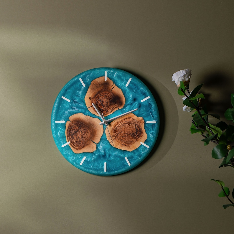 May include: A teal blue resin clock with three wood slices embedded in the resin. The clock has white hands and white numbers around the edge.