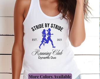 May include: White tank top with a blue graphic that reads "Stride by Stride Running Club Dynamic Duo." The design features two running figures. The text "EST. 2023" is also included. The bottom of the shirt says "More Colors Available."
