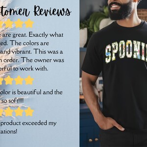 K&ouml;nnte beinhalten: Ein schwarzes T-Shirt mit dem Wort "SPOONIE" in bunten Buchstaben bedruckt. Die Buchstaben sind mit einem Blumenmuster verziert. Das Shirt wird von einer Person mit Bart getragen.