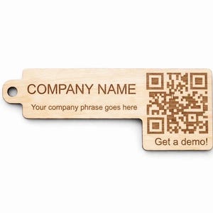 Op de afbeelding: Een lichtgekleurde houten sleutelhanger met een gat voor een sleutelhanger. De tag heeft de tekst "COMPANY NAME" en "Your company phrase goes here" gegraveerd. Een QR-code en de tekst "Get a demo!" zijn ook gegraveerd.
