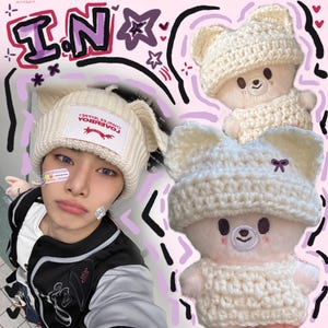 May include: Cream-colored crochet bear hat with attached ears and a matching crochet bear doll. The hat has a rectangular label that reads "LOVEBOK CHARLES TERREY". The bear doll has a smiling face and is wearing a matching crochet sweater.