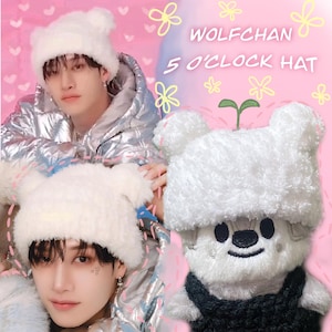 May include: White fuzzy hat with bear ears and a small plant growing from the top. The hat is worn by a person with black hair and a silver jacket. The text "WOLFCHAN 5 O'CLOCK HAT" is written in the background.