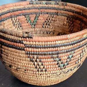 Peut inclure: Un panier tissé à la main de forme arrondie. Le panier présente une couleur beige naturel avec des bandes noires, orange et vertes. Le motif tissé crée une surface texturée. Ce panier décoratif convient au rangement ou à l'exposition.