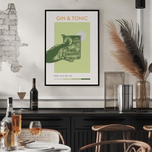 A minimalist Gin Tonic cocktail poster with a green color, also carrying a retro vibe, created using an image of a hand holding a classic cocktail glass, with photo effects, is hanging on a white dining room wall, within a black frame