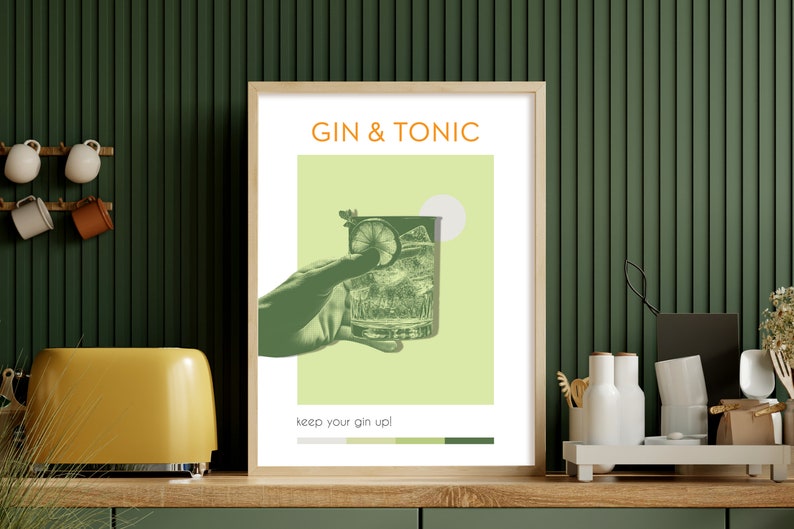 The minimalist green color Gin Tonic print, carries modern vibe effects, a hand holding a glass, leaning against the green wall on the counter of a modern kitchen. There are espresso cups and a toaster on the side.