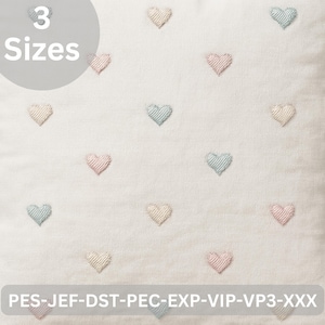 Könnte beinhalten: Ein weißes Kissen mit gestickten Herzen in Pastellfarben: Rosa, Blau und Creme. Das Kissen hat den Text "3 Größen" in einem grauen Kreis. Der Boden des Kissens trägt den Text "PES-JEF-DST-PEC-EXP-VIP-VP3-XXX".