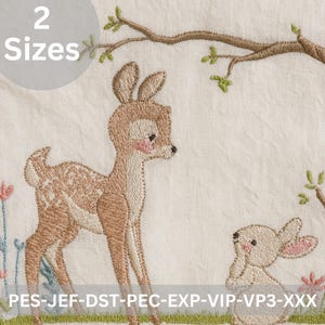 Puede incluir: Diseño bordado con un cervatillo y un conejo, con una rama de árbol encima. El diseño incluye el texto "2 Sizes" en un círculo. La imagen está sobre una tela color crema, con detalles florales y de follaje.