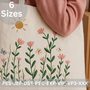 May include: Cream-colored tote bag with an embroidered floral design. The design features pink flowers, green stems, and yellow butterflies, with a gold sun in the upper left corner. The text "6 Sizes" is above the design.