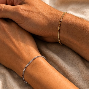 May include: A gold-toned metal chain bracelet and a silver-toned metal chain bracelet. Both bracelets feature a delicate, interlocking link design and are worn on the wrists. The gold bracelet is on the upper wrist, while the silver bracelet is on the lower wrist.