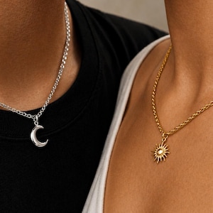 Può includere: Due collane, una con un ciondolo a mezzaluna argentata e l'altra con un ciondolo a forma di sole dorato. Il ciondolo a forma di luna è su una catena d'argento, e il ciondolo a forma di sole è su una catena d'oro.