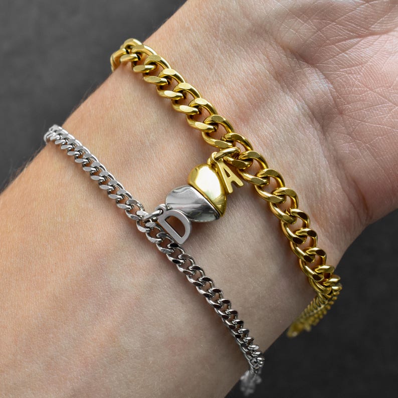 May include: Two curb chain bracelets, one gold-toned and one silver-toned, featuring a split heart charm. The gold chain has a gold letter A attached to the heart, and the silver chain has a silver letter D attached to the heart piece.