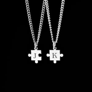 Pode incluir: Dois colares de prata com pingentes de peça de quebra-cabeça. Os pingentes são gravados com as letras "J" e "K".