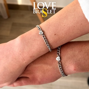 May include: Two silver chain bracelets, each featuring a heart-shaped charm with the inscription "I love you." The bracelets are displayed on wrists, with the text "LOVE BRASLET" visible in the background.