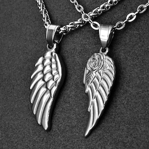 May include: Two silver-colored pendant necklaces. One pendant is a wing design, the other a wing with a rose. Both are on a silver chain. The pendants are detailed with feather-like textures.