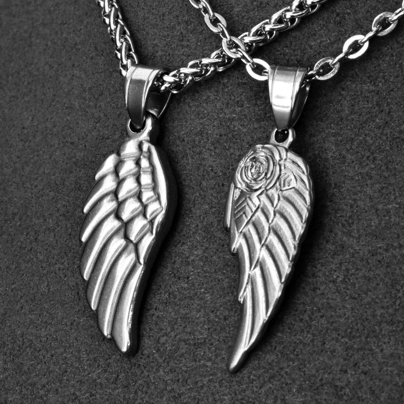 May include: Two silver-colored pendant necklaces. One pendant is a wing design, the other a wing with a rose. Both are on a silver chain. The pendants are detailed with feather-like textures.