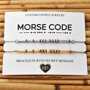 May include: Two Morse code bracelets, one silver and one gold, displayed on a white card. The card reads "CUSTOM COUPLE JEWELRY" and "BRACELETS WITH SECRET MESSAGE". The bracelets are on a bamboo background.