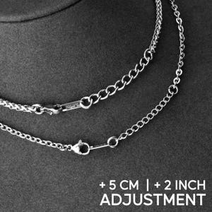 May include: Close-up of two silver necklaces with different chain styles. One chain is a curb style, and the other is a cable chain. The necklaces have a clasp closure. The text at the bottom reads "+5 CM | +2 INCH ADJUSTMENT."