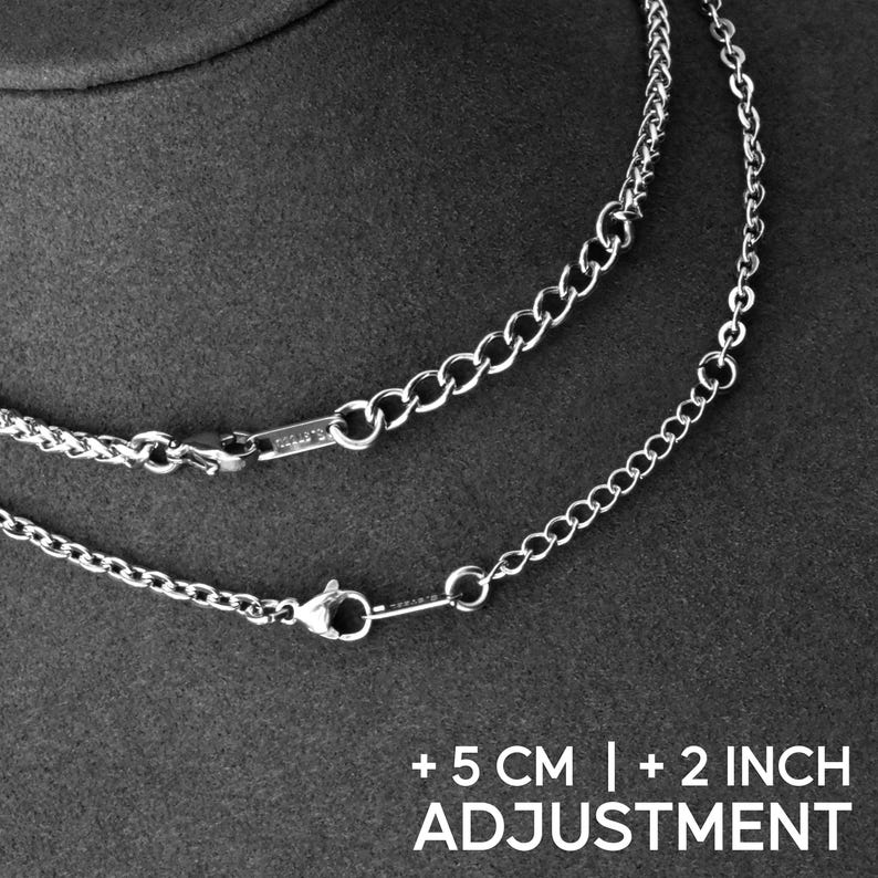 May include: Close-up of two silver necklaces with different chain styles. One chain is a curb style, and the other is a cable chain. The necklaces have a clasp closure. The text at the bottom reads "+5 CM | +2 INCH ADJUSTMENT."