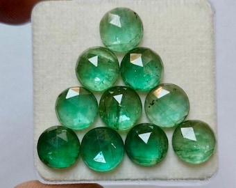 May include: A collection of ten round, faceted green gemstones arranged in a triangular formation on a white square display card. Each stone features a rose-cut surface with visible internal inclusions and a vibrant emerald green hue.