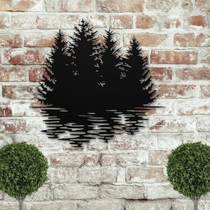 May include: Black metal wall art showing a forest scene with trees and their reflection in water. The artwork is mounted on a brick wall. Two green, round topiary bushes are on either side of the artwork.