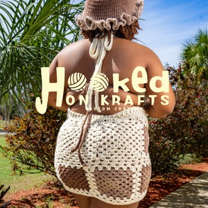 May include: A crocheted mini dress in brown and white, featuring a halter top and a skirt with a geometric pattern. The model is wearing a brown crocheted hat with a ruffled brim. The text "Hooked On Krafts Custom Crochet" is visible on the dress.
