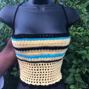 May include: A handmade crochet top in a bustier style, featuring a black, light blue, and yellow striped pattern. The top has a scalloped black trim and thin black straps. The open weave design adds a unique texture to this garment.