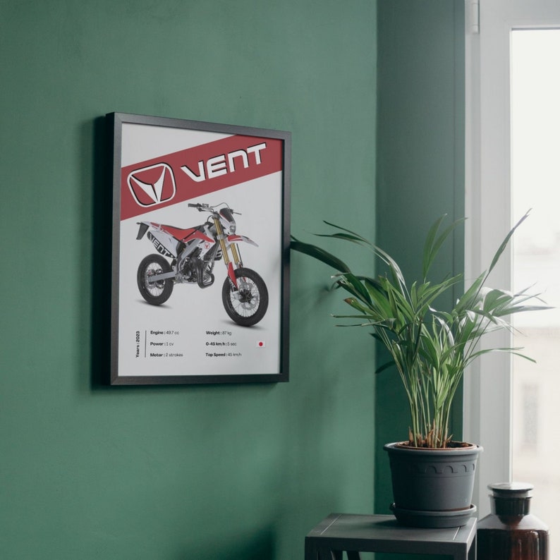 May include: A framed poster featuring a red and white dirt bike with the word "VENT" in bold red letters. The poster includes specifications for the bike, including the year, engine size, power, weight, 0-40 km/h time, and top speed.