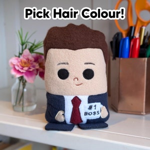 May include: A plush toy of a person wearing a blue suit and a red tie. The toy has brown hair and a name tag that says "#1 BOSS".