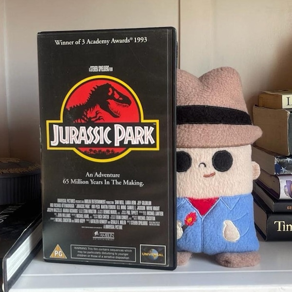 Jurassic Park plush with VHS art collectable. Dr Alan Grant dinosaur soft toy figure for display. Retro movie art with handmade plushie