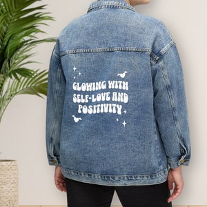 May include: A blue denim jacket with a white graphic on the back that says "Glowing with self-love and positivity".