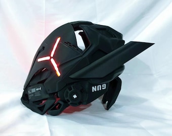 Puede incluir: Casco futurista negro con un diseño en forma de cruz roja iluminada en la parte delantera. El casco tiene características angulares, una visera y la palabra "GUN" impresa en el lateral. El casco es probablemente para cosplay o un evento temático.