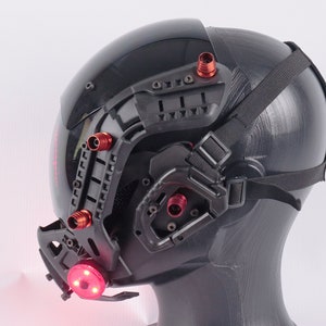 May include: A black helmet with a red light and a black strap. The helmet has a variety of attachments and is designed for tactical use.