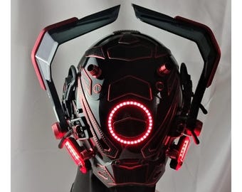 Op de afbeelding: Een futuristische zwarte helm met rode accenten en gloeiende rode lichten. De helm heeft een cirkelvormig licht rond het gezicht en extra lichten aan de zijkanten. Het ontwerp bevat hoekige vormen en een glanzende afwerking, wat een sci-fi esthetiek creëert.