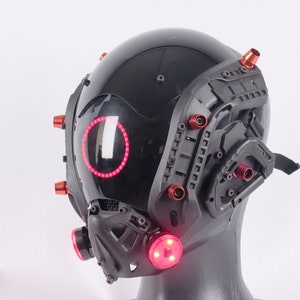 May include: A black helmet with red lights and a black and gray face mask. The helmet has a clear visor and multiple red accents.